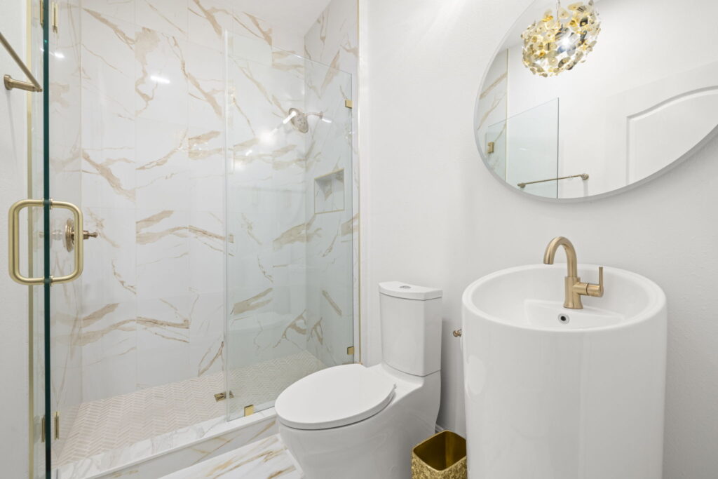 Modern bathroom with marble shower and gold accents.