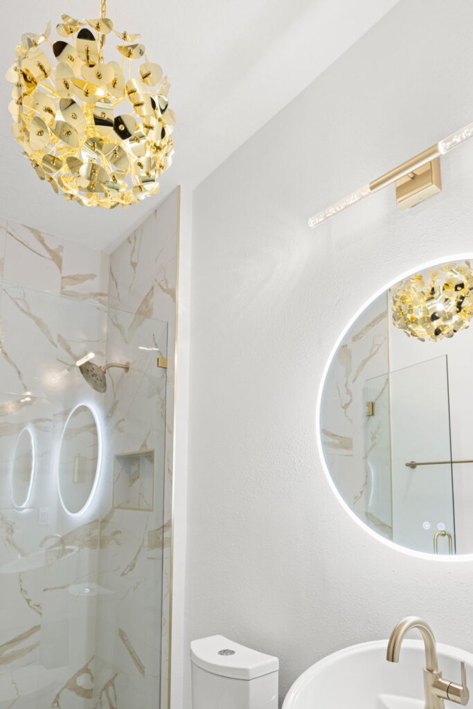 Modern bathroom with gold pendant light and round mirror.