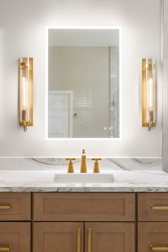 Modern bathroom with illuminated mirror and gold fixtures.
