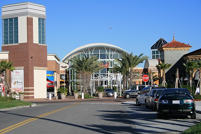 Entrance of a bustling shopping center with palm trees.