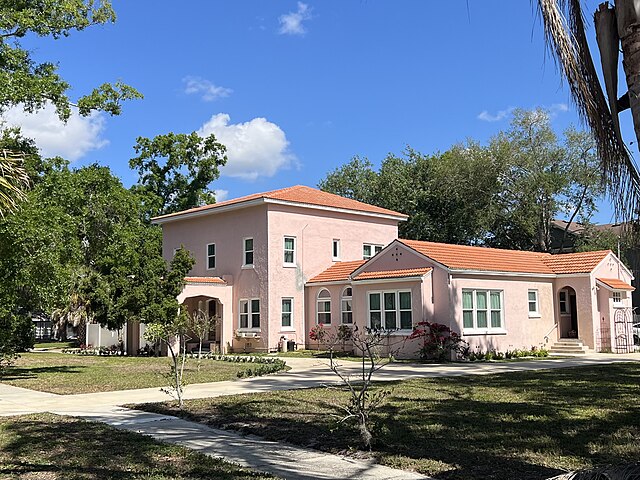 Pink house with red tile roof under blue sky.
