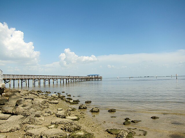 Pier extending over calm waters under a partly cloudy sky.