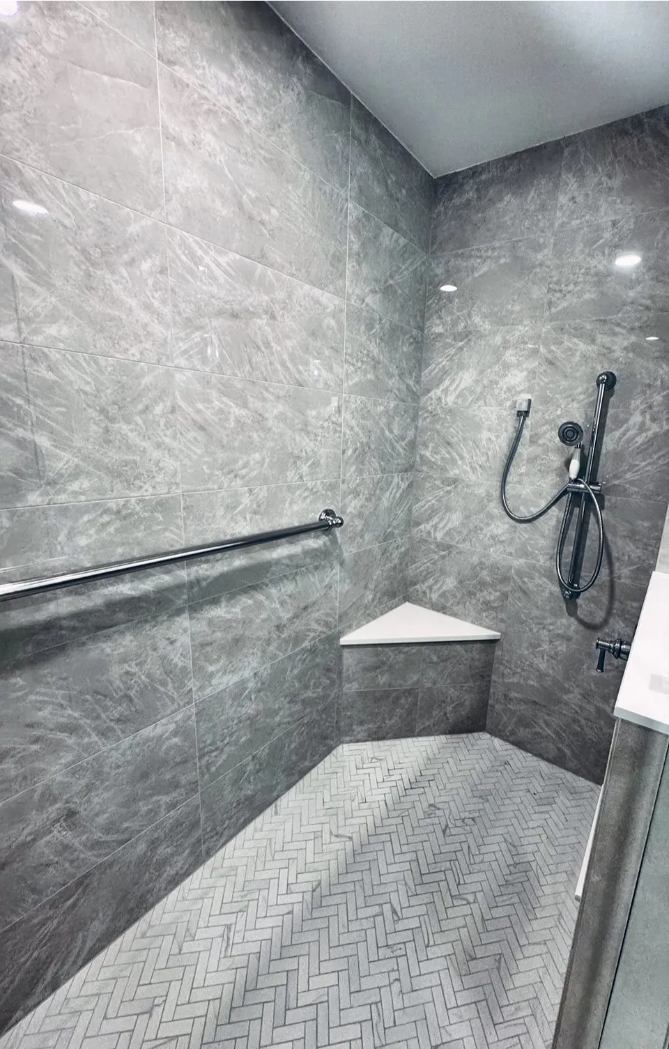 Corner shower bench with white slab seat, long grab bar, and handheld on slide bar over a marble herringbone floor in an Indian Rocks Beach shower
