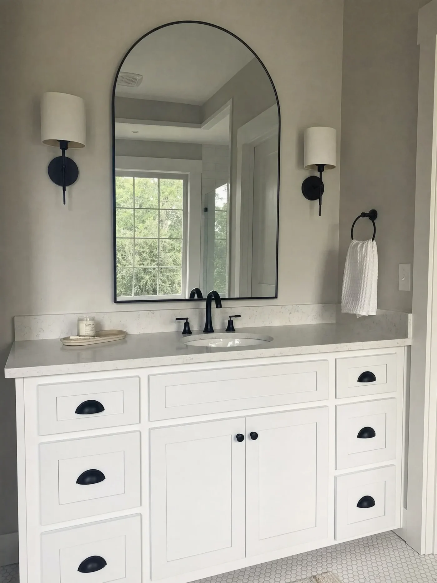 Arched mirror with matte black frame and wall sconces above white shaker vanity with marble countertop in Seminole FL bathroom by CMK Construction