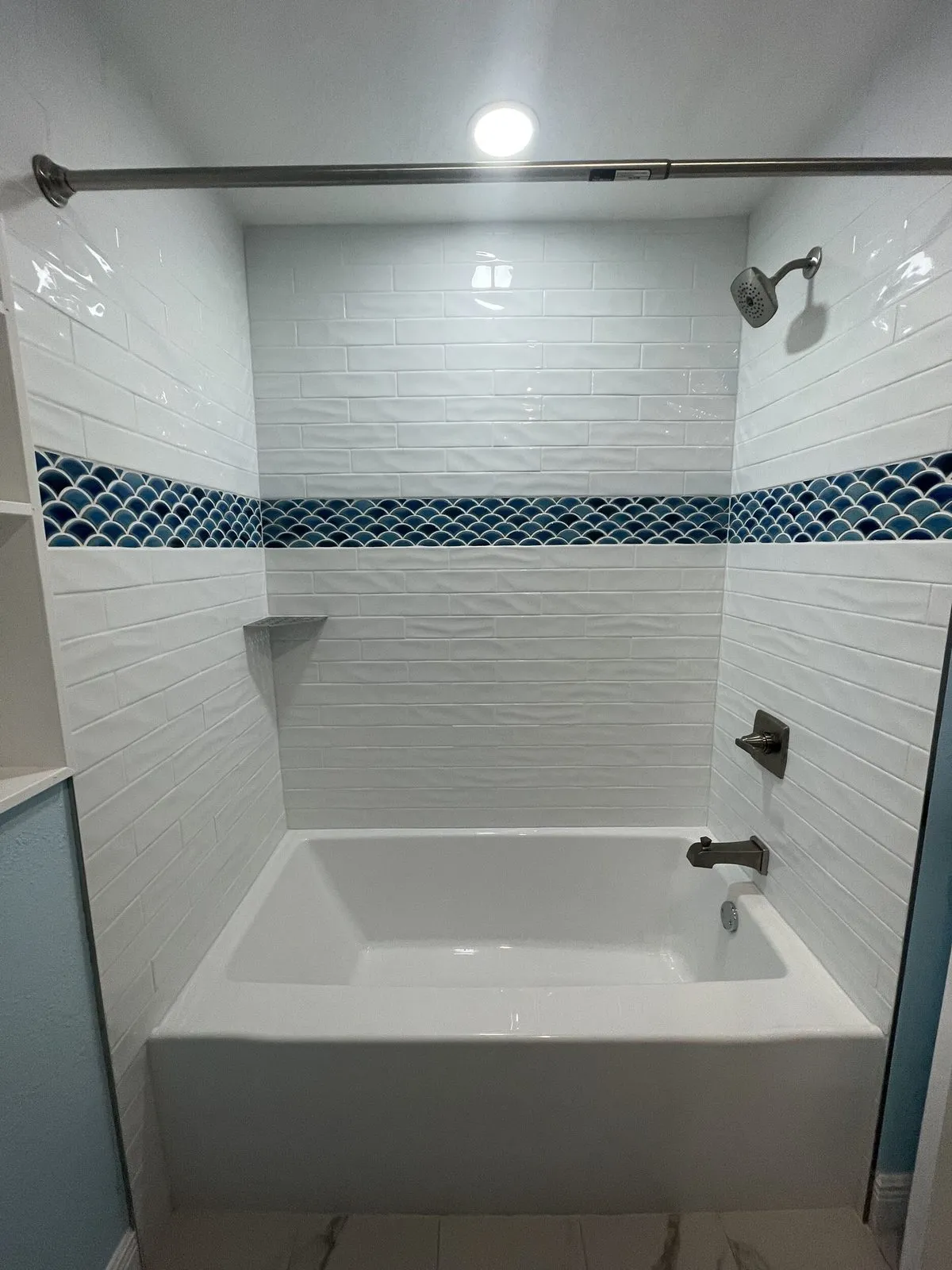Bathroom after remodeling in Clearwater by CMK with new white tub, textured white subway tile surround, and blue fish scale accent band