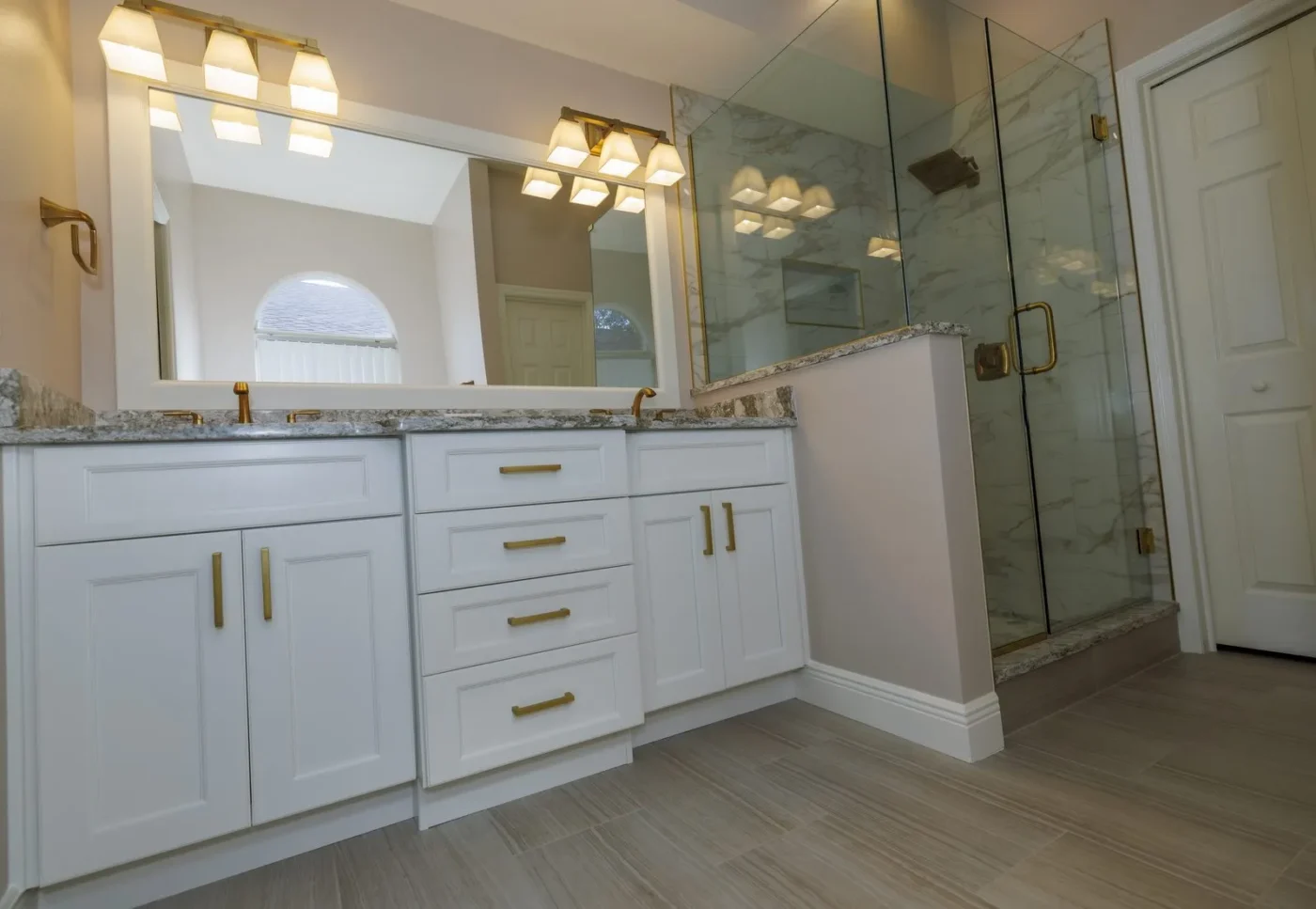 Primary bathroom after remodeling in Land O Lakes by CMK with white double vanity, quartz tops, brass hardware, and frameless glass shower in marble look porcelain