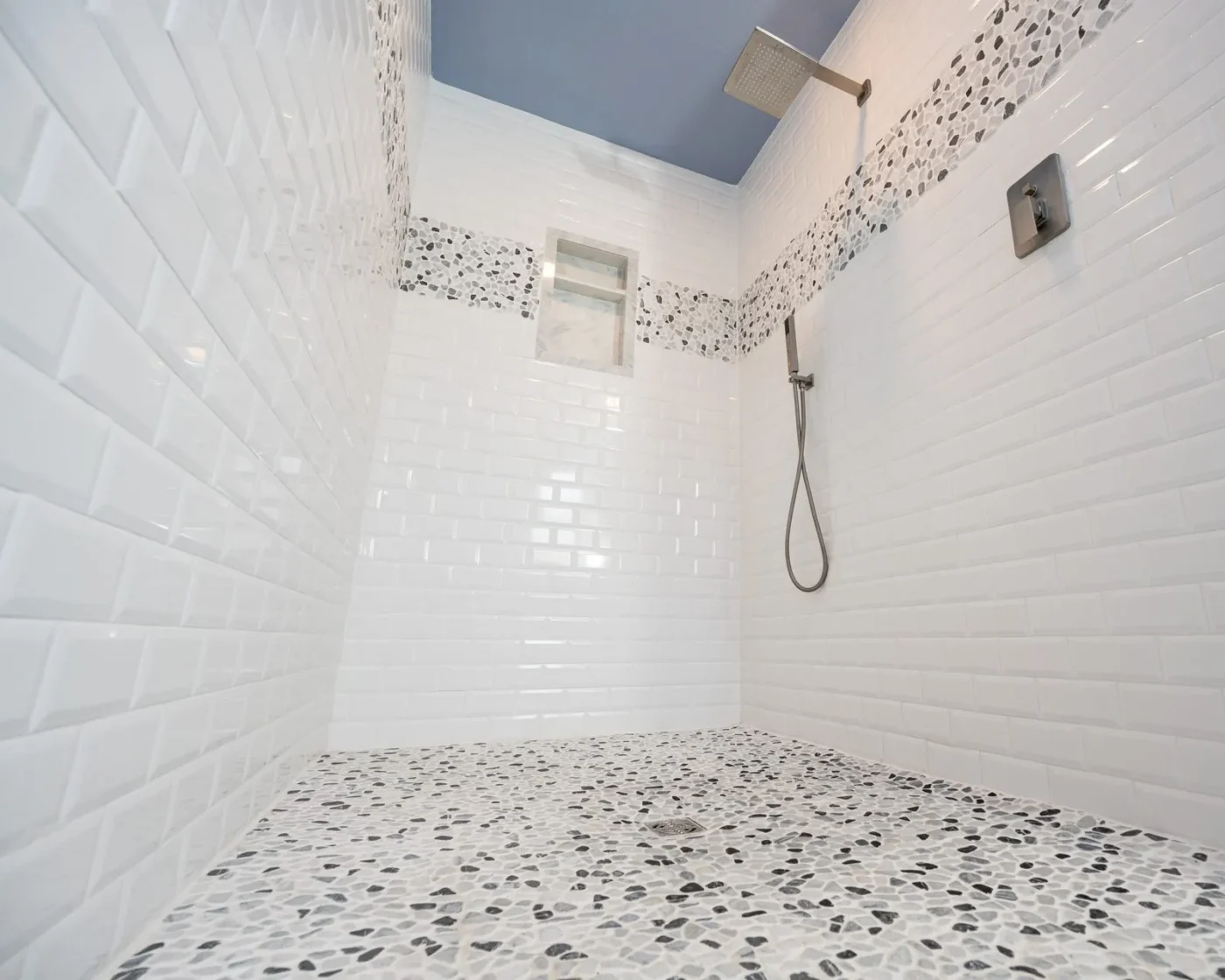 Walk in shower after remodeling in Sarasota by CMK with beveled subway tile, pebble mosaic floor and accent band, marble trimmed niche, and rain shower head