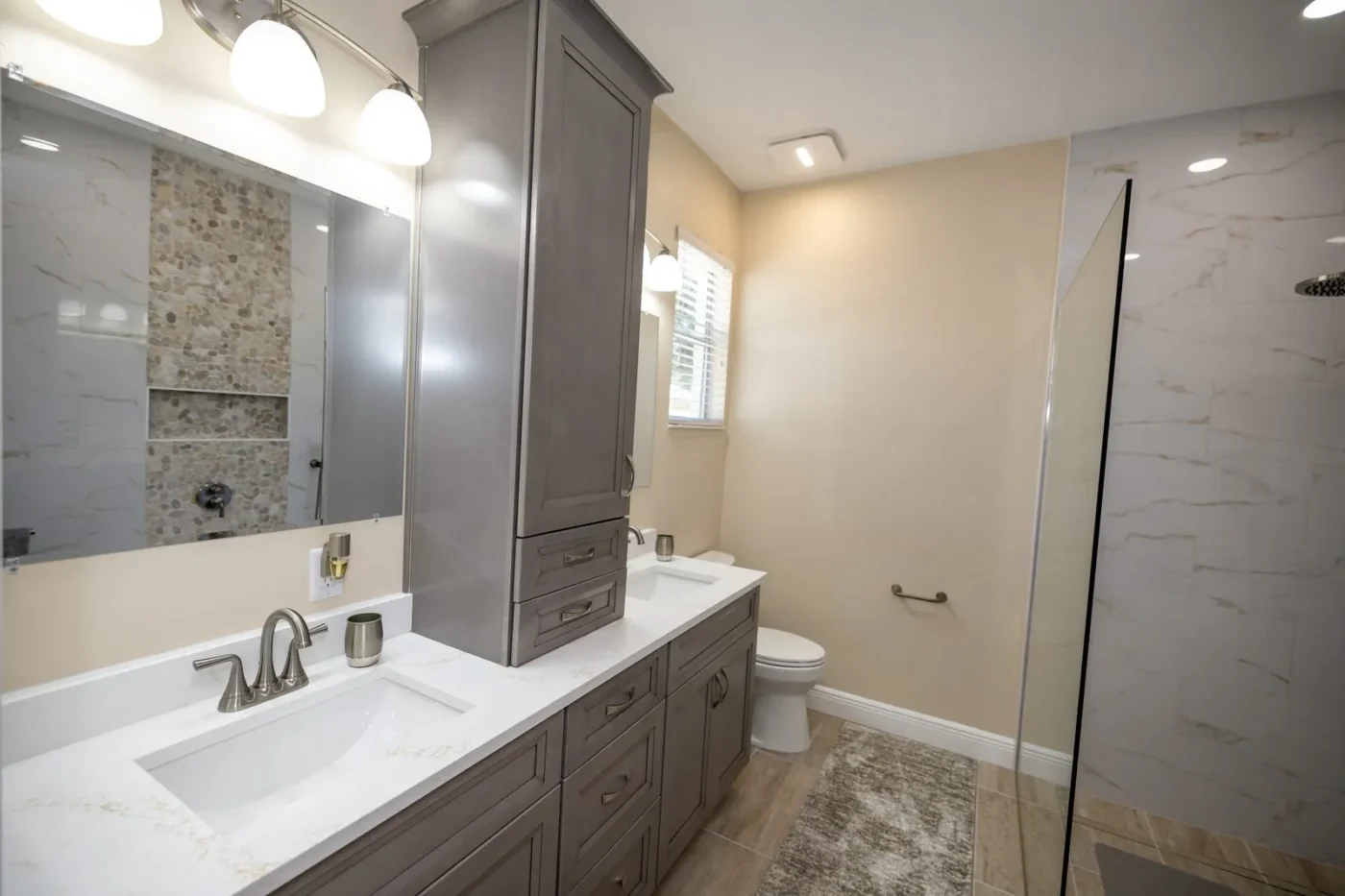Gray double vanity with tower cabinet and quartz tops after bathroom remodeling in Tampa by CMK