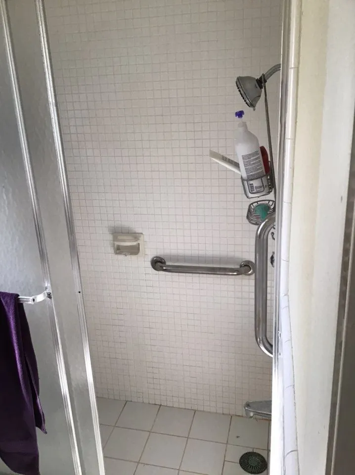 Shower before remodeling in Sarasota with dated small format tile, add on grab bars, and framed sliding door