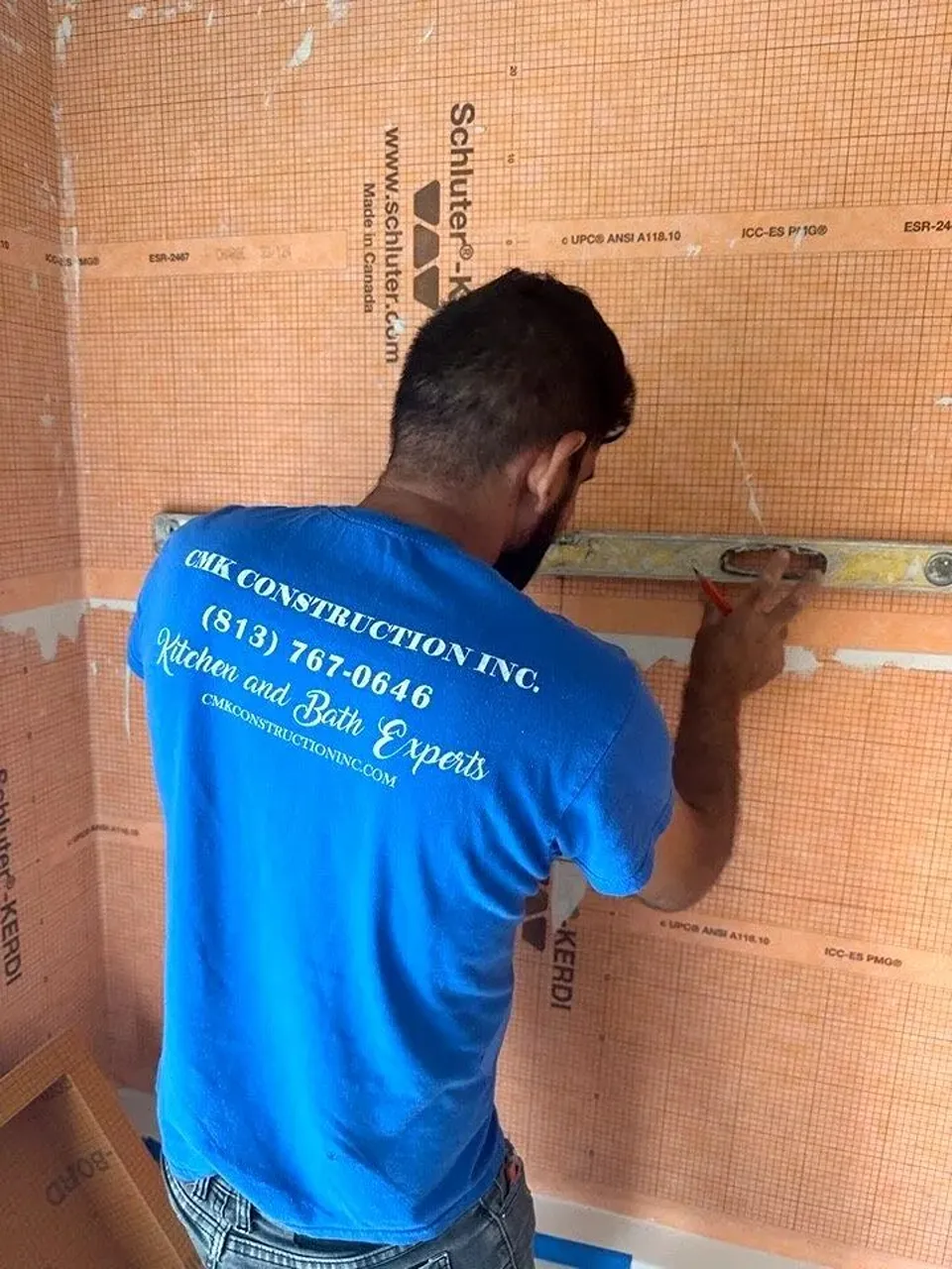 Safety Harbor bathroom remodel showing orange Schluter waterproofing membrane on shower walls while a CMK installer checks the surface with a level.