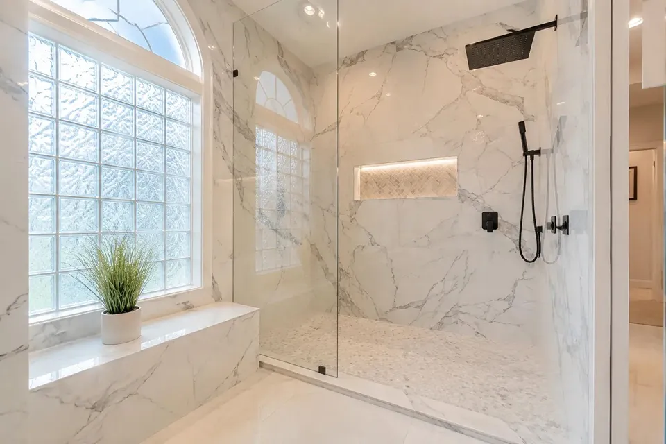Tampa Palms bathroom remodel with marble look shower tile, glass enclosure, a built in niche, bench, and black shower fixtures.