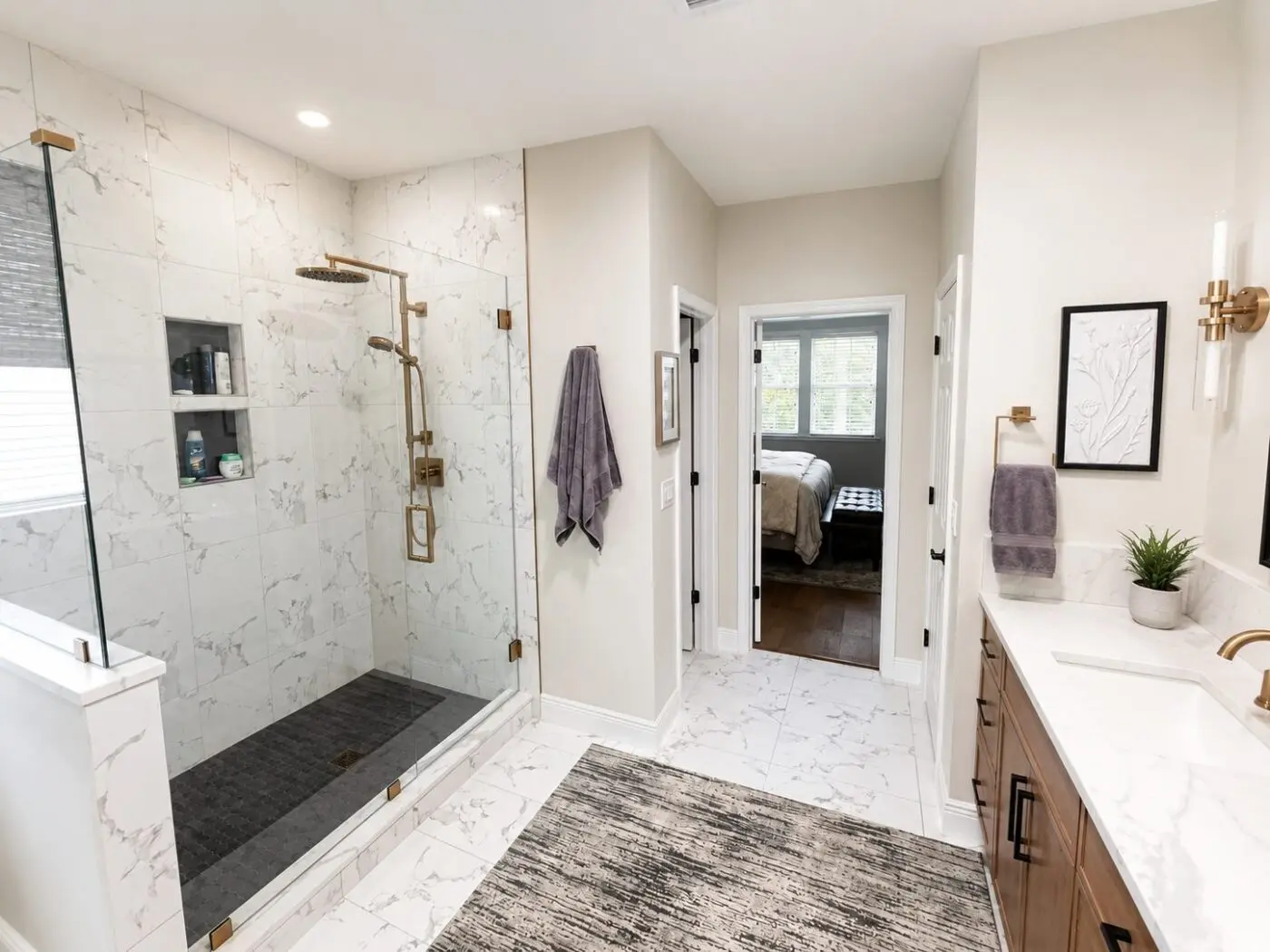 Master bathroom with marble look shower walls, dark contrast shower pan, marble look floor tile, and warm metal fixtures in a Lakewood Ranch remodel