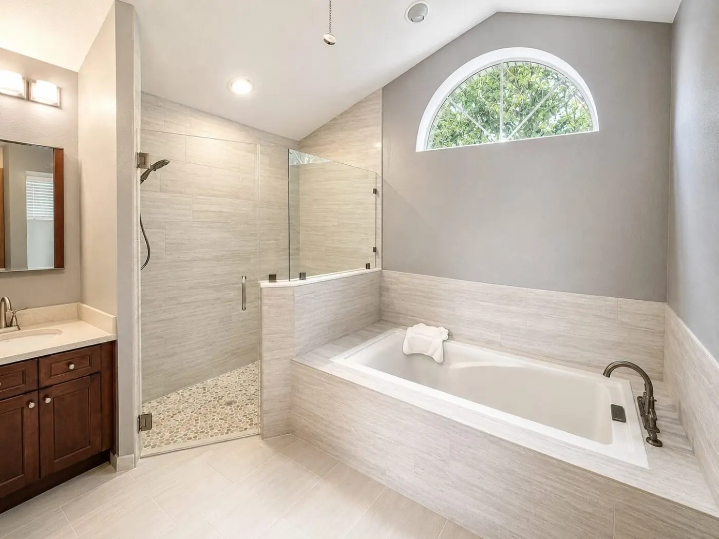 Master bathroom with light stone look tile on shower walls and tub deck, pebble shower floor, and arched window in an Odessa remodel