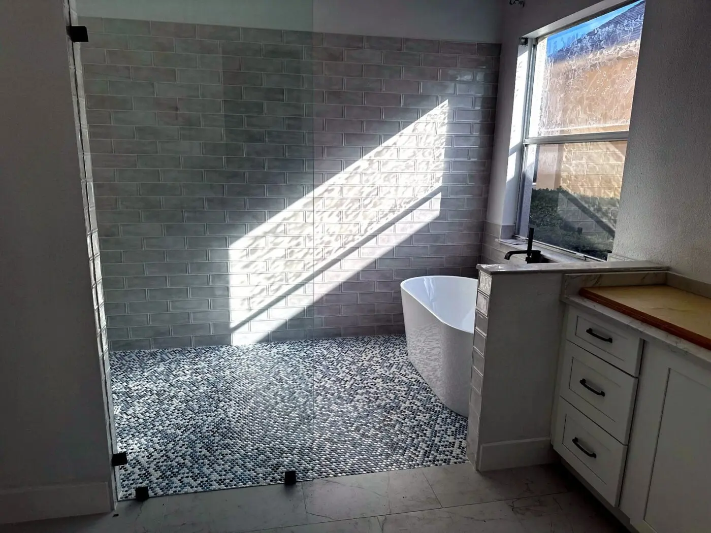 Walk in shower with gray handmade look subway wall tile, blue toned penny round mosaic floor, and freestanding tub in an Odessa master bathroom remodel