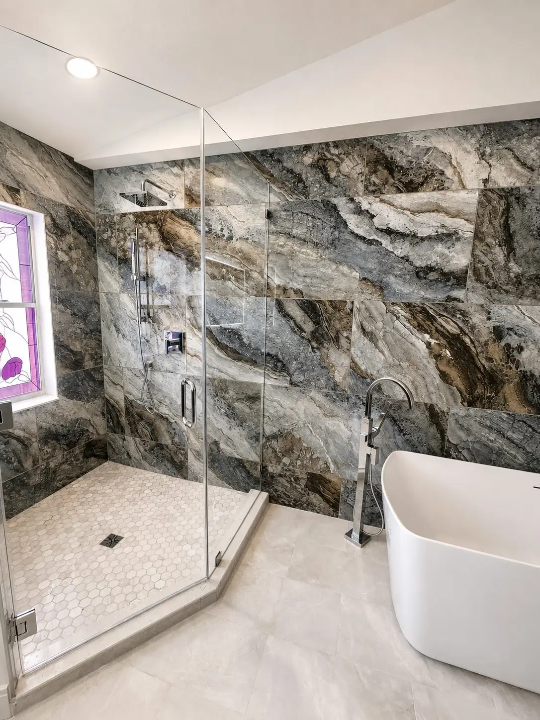 Shower with dramatic blue gray exotic stone look wall tile, hexagon mosaic shower floor, and freestanding tub in an Oldsmar master bathroom remodel