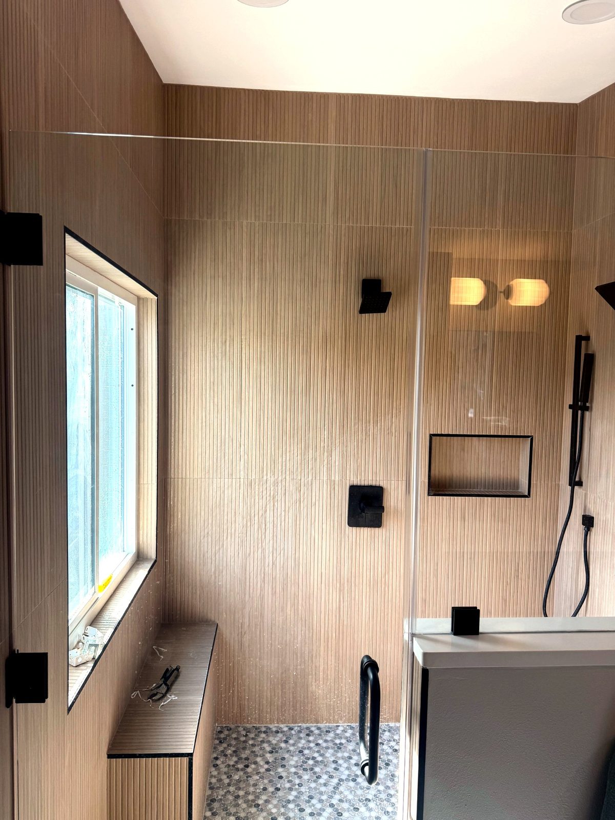 Master shower with fluted wood look wall tile, tiled bench, matte black fixtures, and penny round mosaic floor in a Sarasota bathroom remodel