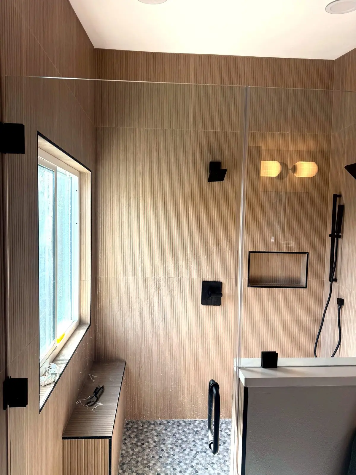 Master shower with fluted wood look wall tile, tiled bench, matte black fixtures, and penny round mosaic floor in a Sarasota bathroom remodel