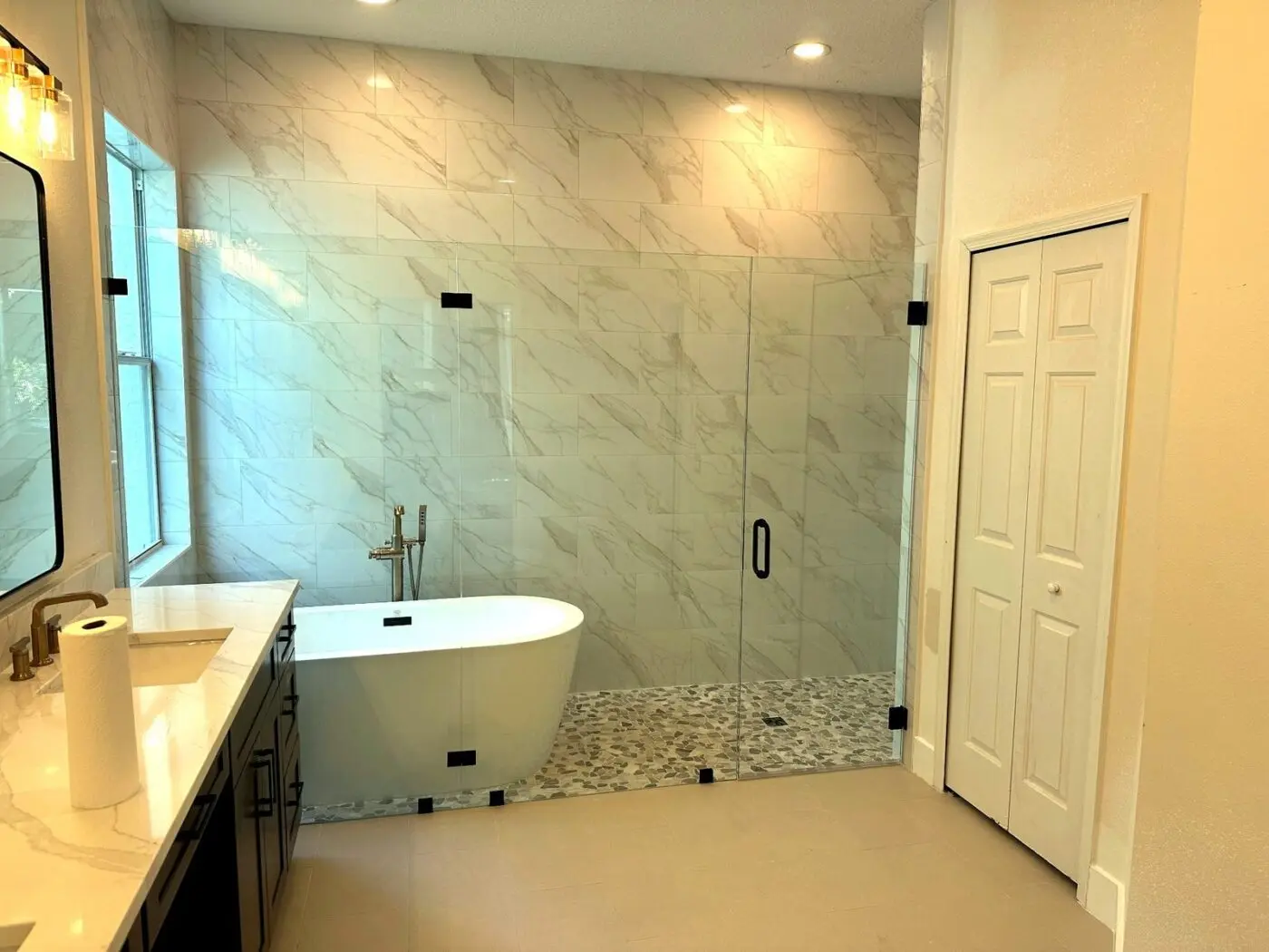 Master bathroom with gold veined large format shower walls, pebble mosaic shower floor, and freestanding tub in a South Tampa remodel