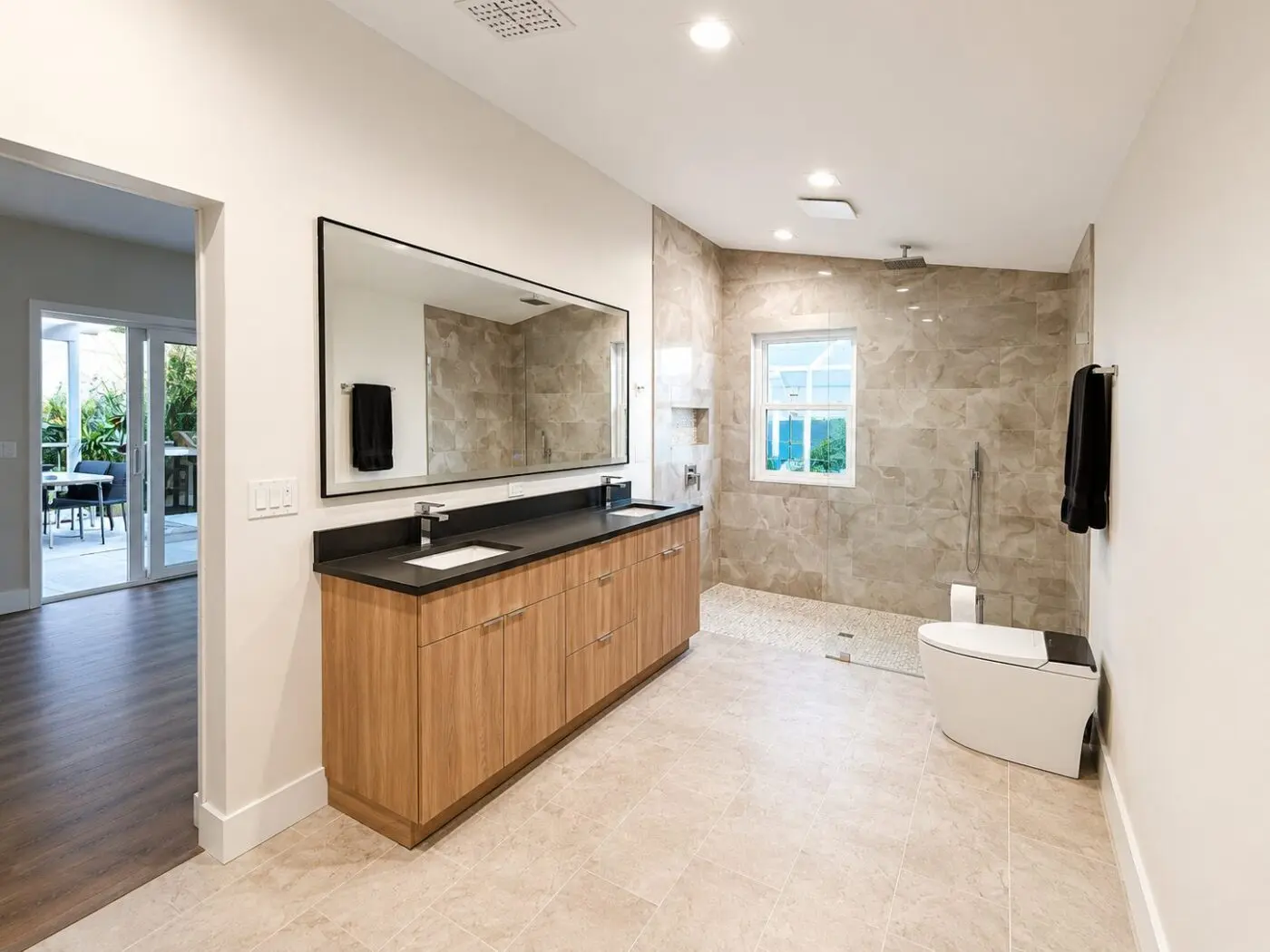 Open master bathroom with warm earth tone stone look shower walls, wood grain vanity, and stone look floor tile in a St. Petersburg remodel