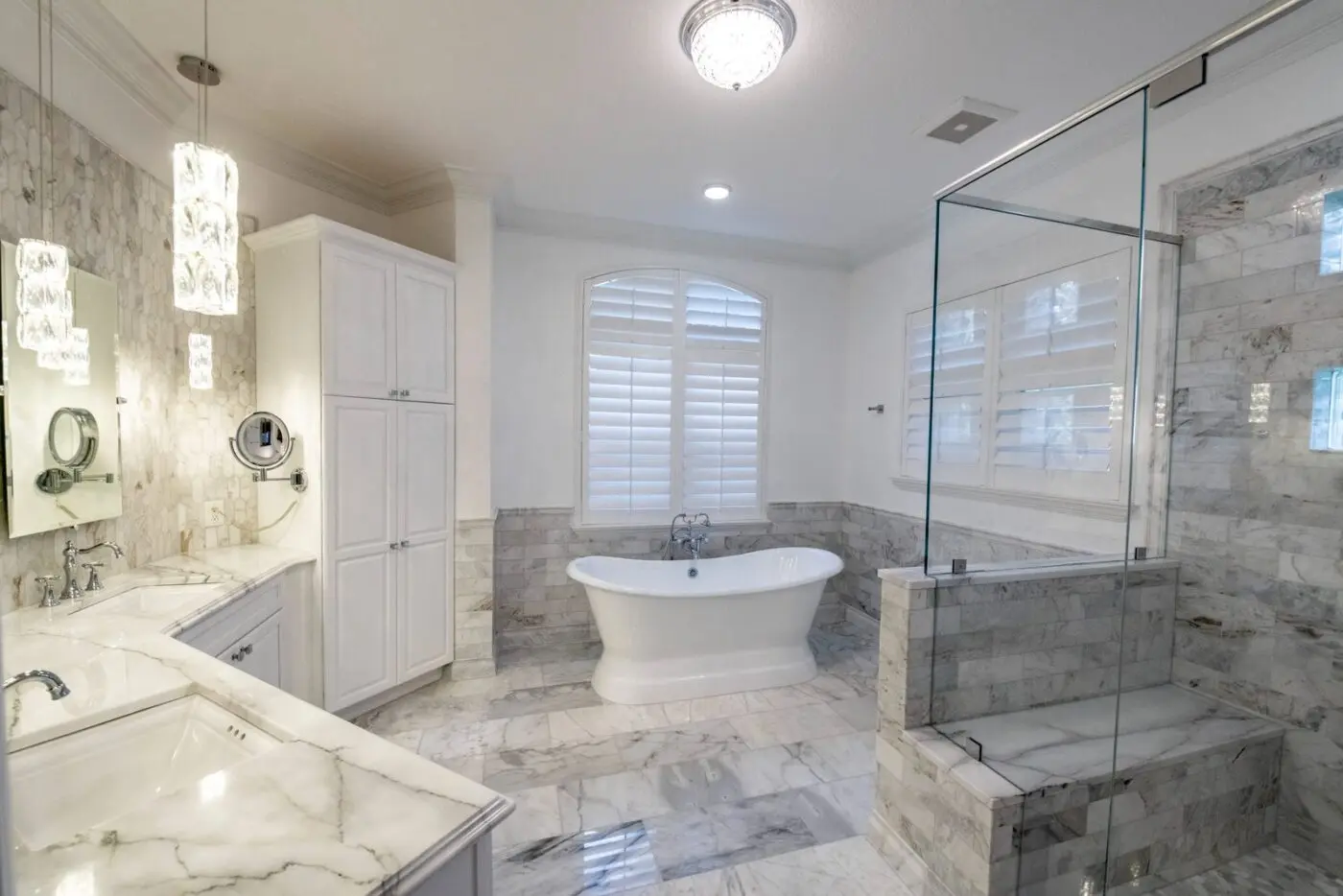 Classic Tampa master bathroom with natural marble subway wainscot, marble floor, picket mosaic vanity wall, freestanding pedestal tub, and glass shower