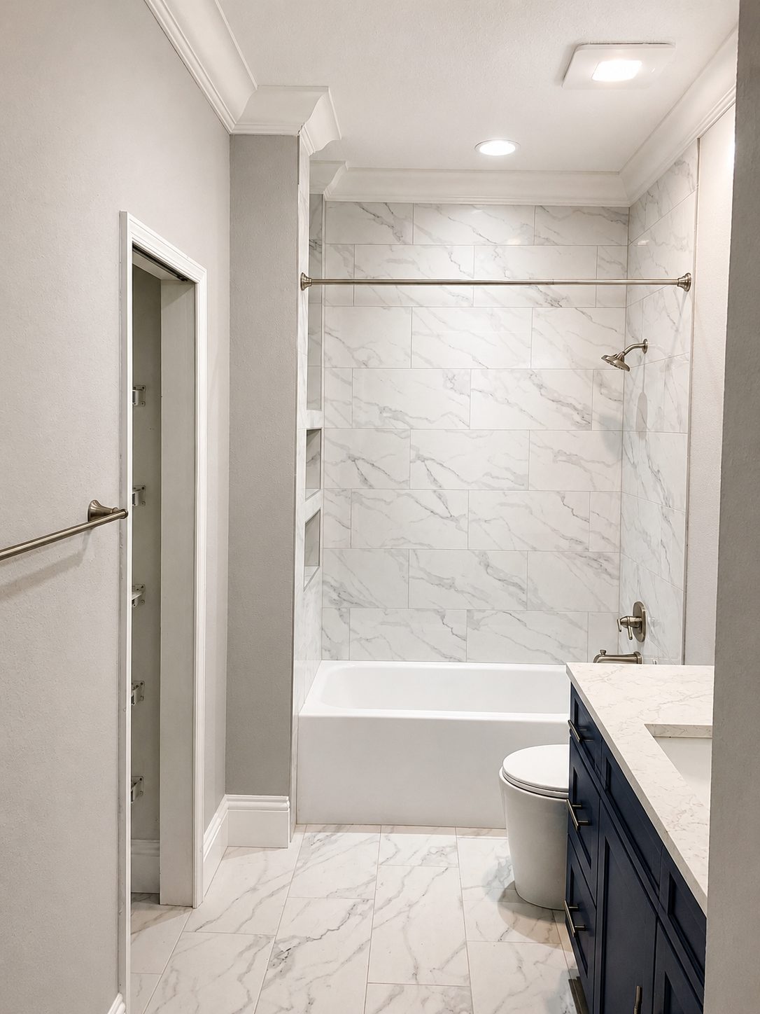 Guest bathroom with gray veined marble look tile on the tub surround and floor with stacked niches and a dark vanity in a Wesley Chapel remodel
