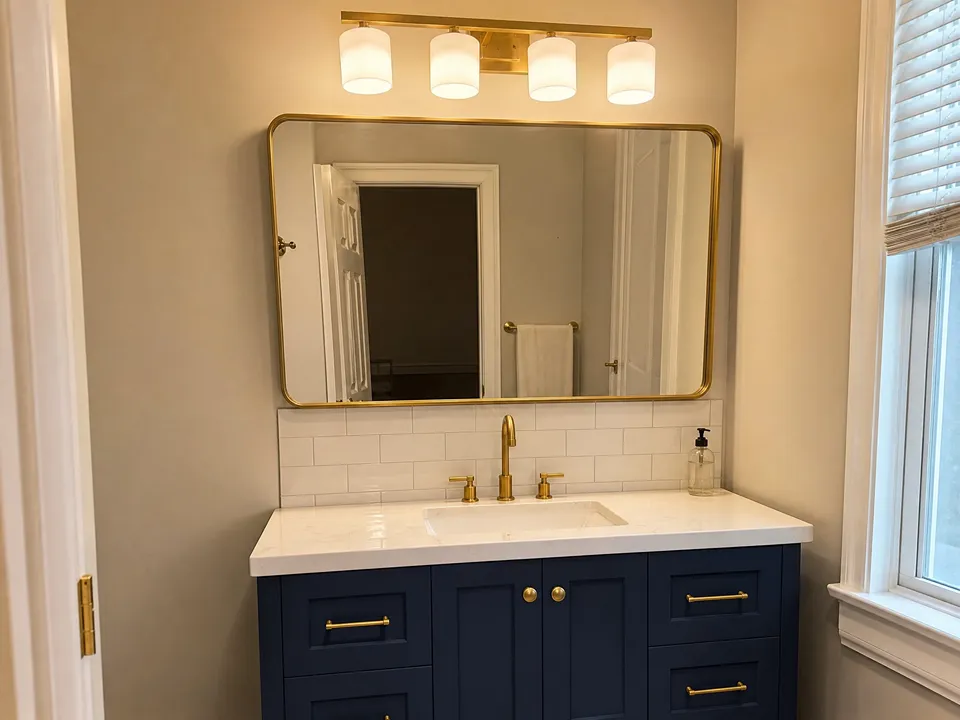 Brushed gold four-light vanity bar with frosted glass shades above a framed mirror, a transitional lighting idea for Dunedin bathrooms