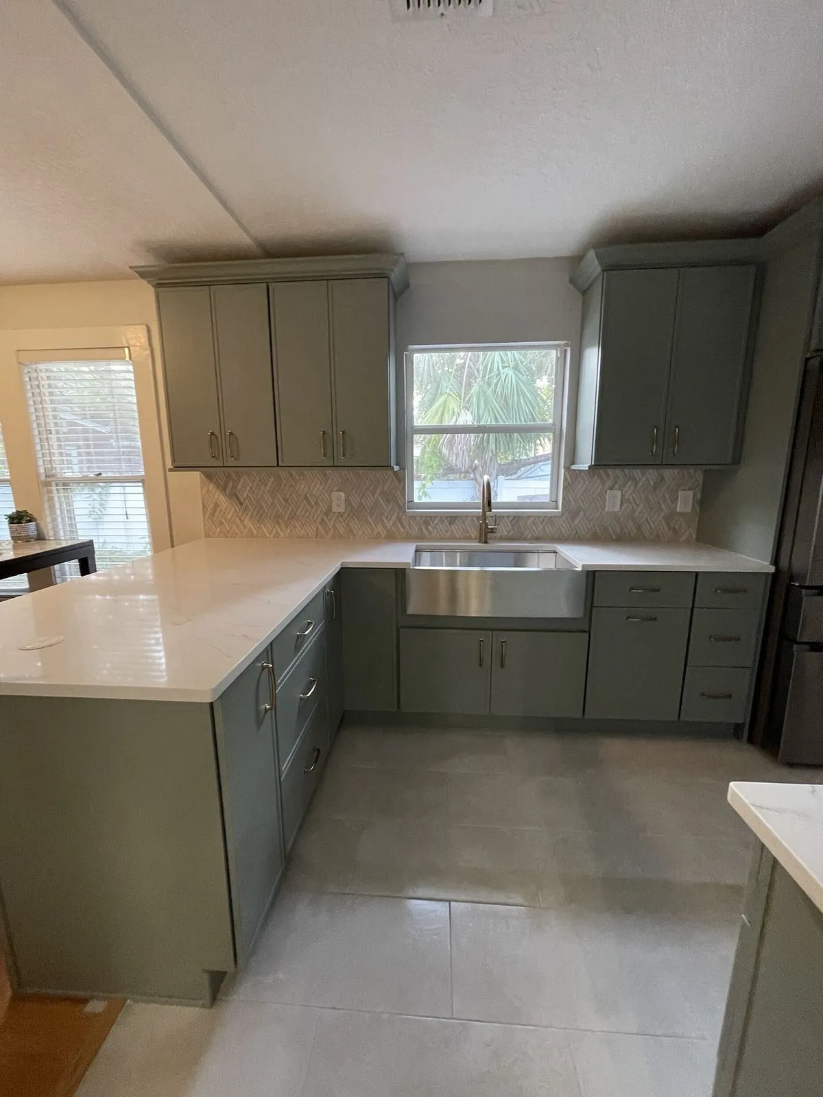 Sage green kitchen cabinets with Cambria quartz peninsula and stainless farmhouse sink in a Tampa kitchen remodel