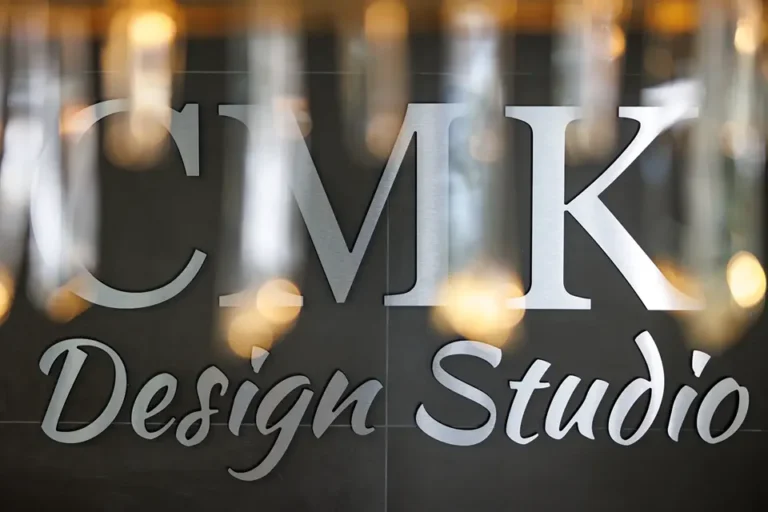Close-up view of a sign that reads CMK Design Studio with hanging lights blurred in the foreground.