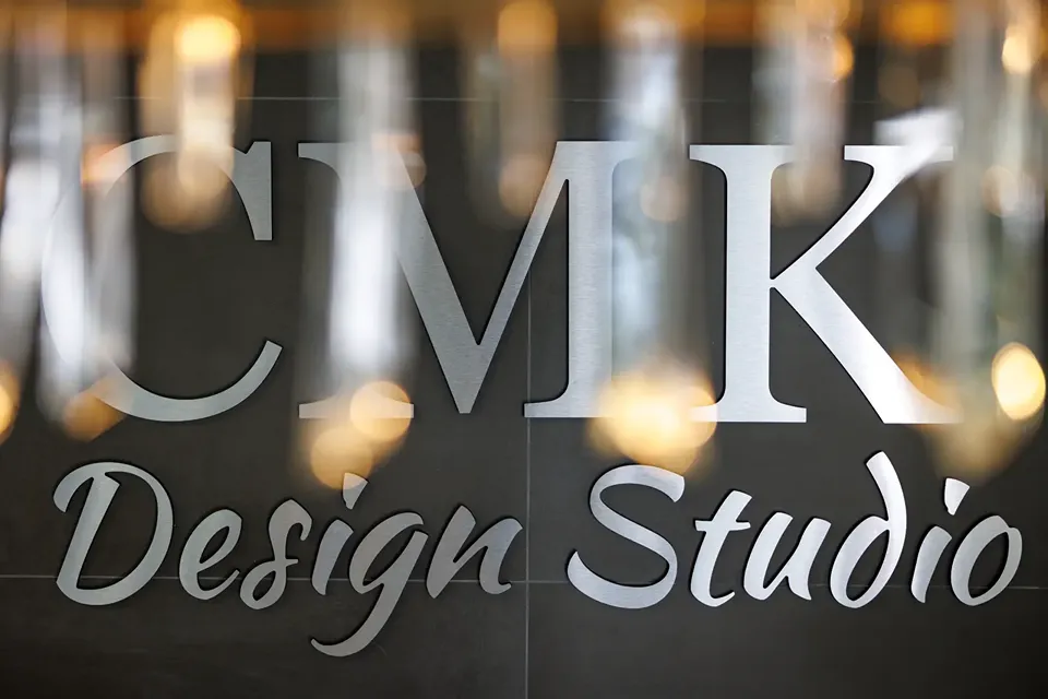 Brushed metal CMK Design Studio sign mounted on a dark large-format tile wall inside the Tampa showroom