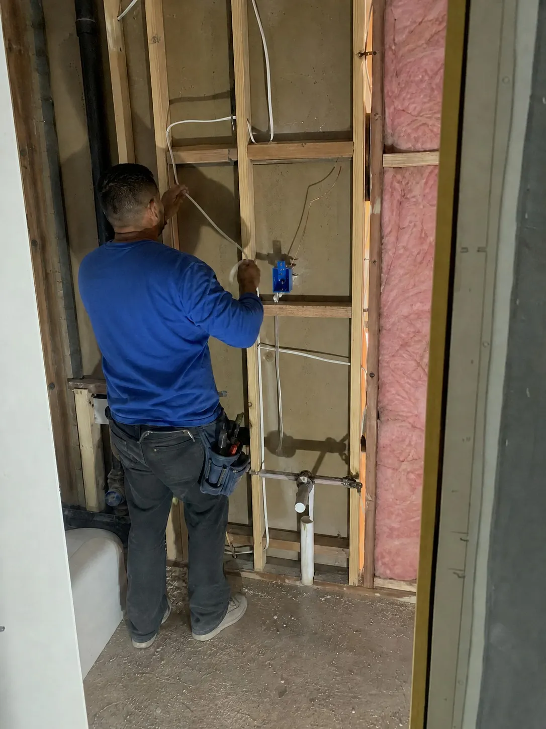 Electrician pulling Romex wire through open wall studs for bathroom mirror junction box during rough in phase in Clearwater FL by CMK Construction