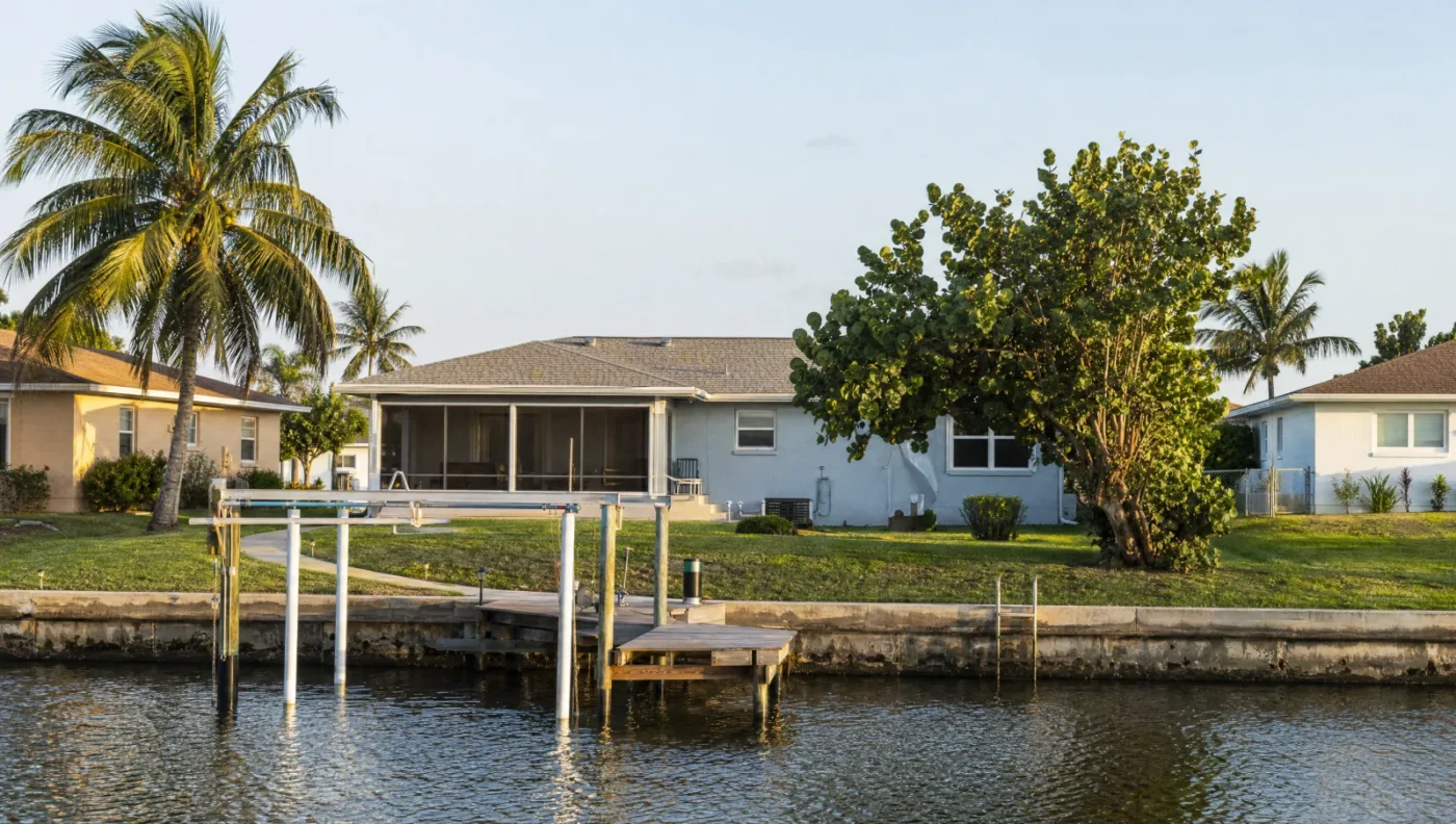 Rear view of a 1980s single-story ranch home on a Pinellas County canal lot with a screened lanai, a seawall, a small dock and an empty boat lift