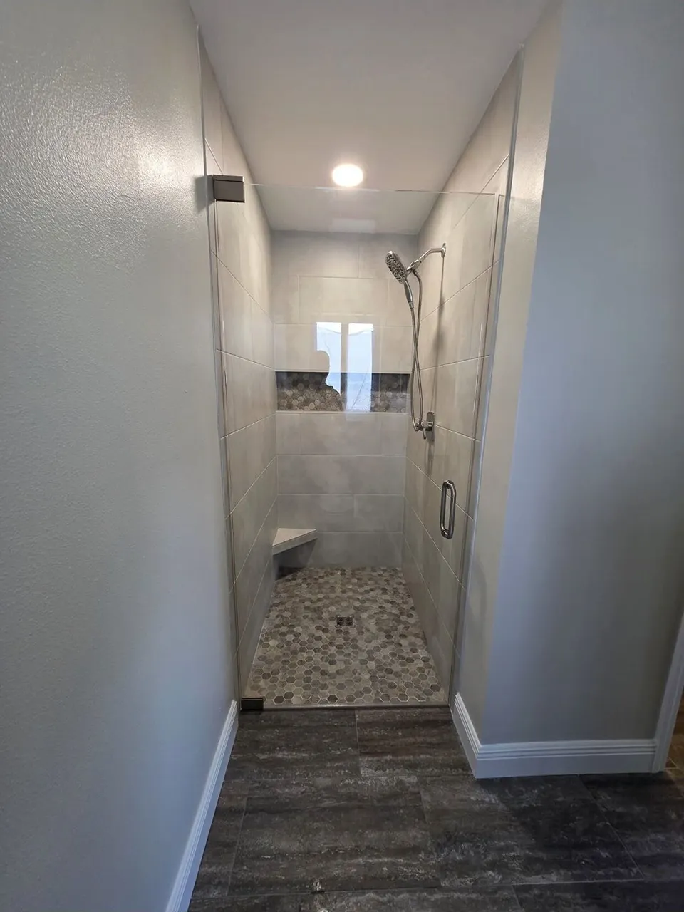 Floating corner shower seat above a hex stone mosaic floor with matching niche band in a Wesley Chapel shower