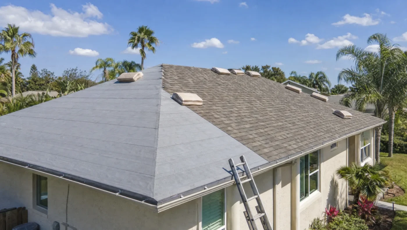 Roof replacement in progress on a 1990s Florida stucco home with gray synthetic underlayment on one side of the hip roof, new architectural shingles on the other and shingle bundles along the ridge