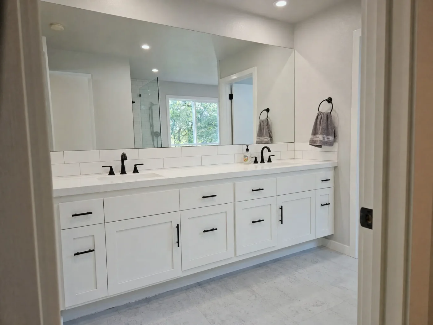 Large frameless wall to wall mirror above white floating double vanity with matte black hardware in Clearwater FL bathroom remodel by CMK Construction