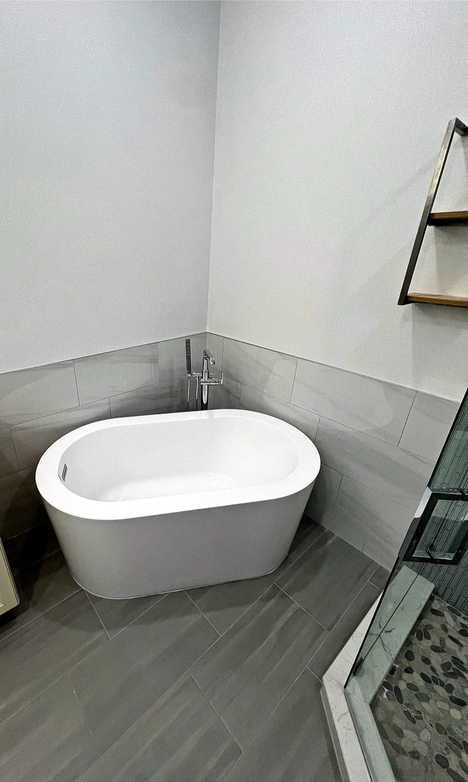 Compact freestanding oval soaking tub in a corner with a chrome floor filler and gray tile wainscot in a smaller Siesta Key bathroom remodel