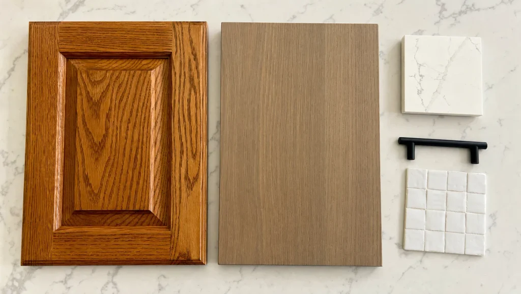 Honey oak raised-panel cabinet door next to a rift-sawn white oak flat-panel door with a quartz sample, black pull and white zellige tile