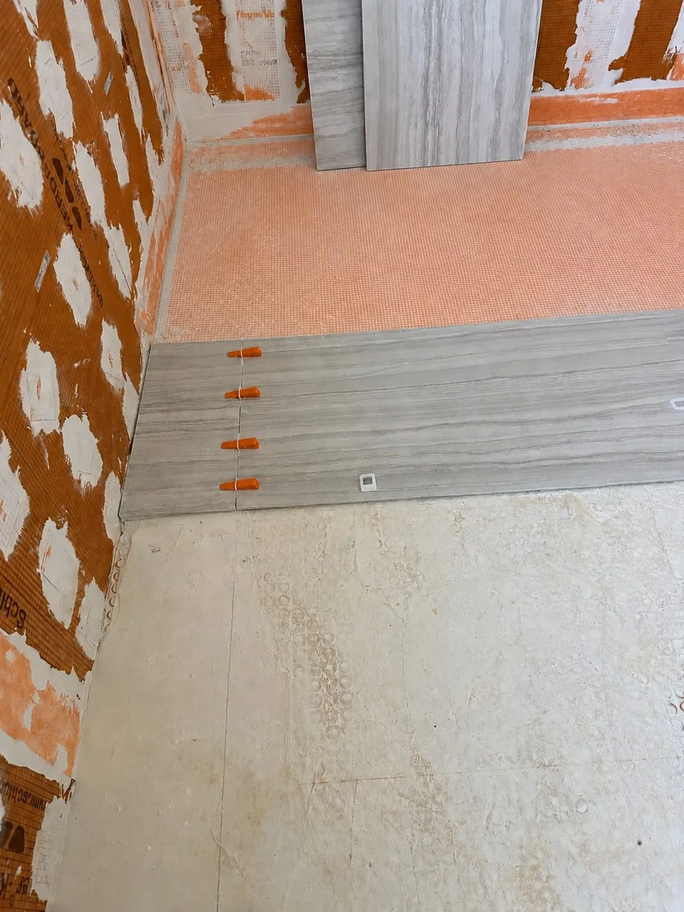 Curbless shower transition with Schluter Kerdi membrane meeting new porcelain floor tile in a Tampa bathroom remodel