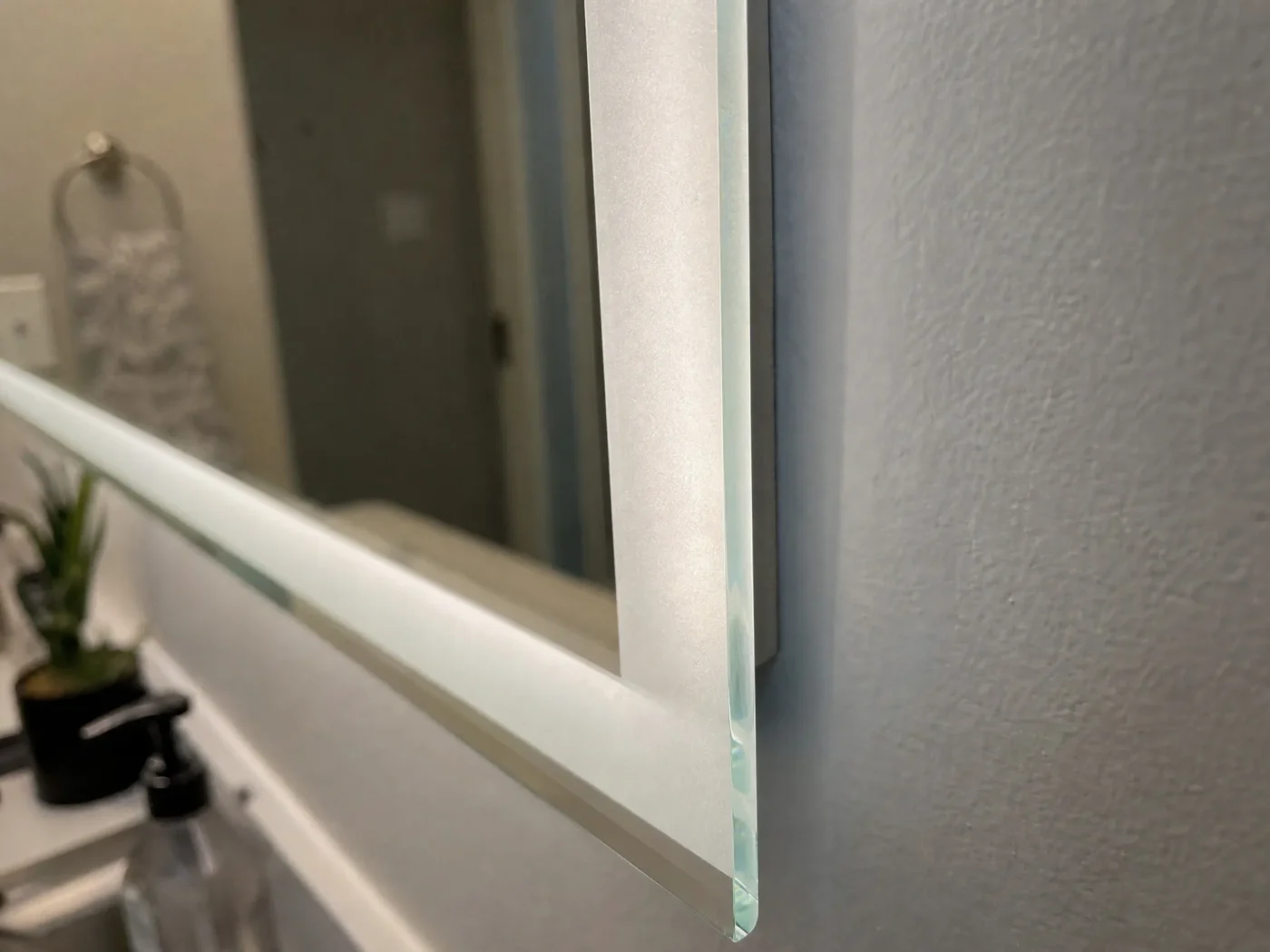 Close up of LED bathroom mirror frosted glass edge showing soft white light glow detail in Tampa FL remodel by CMK Construction