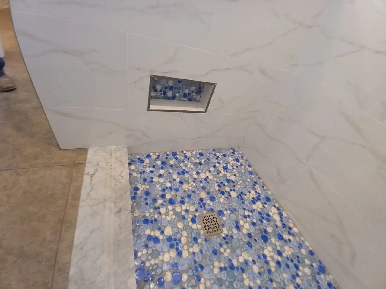 Low placed shower niche with blue pebble contrast tile matching the shower floor in a Land O Lakes remodel by CMK