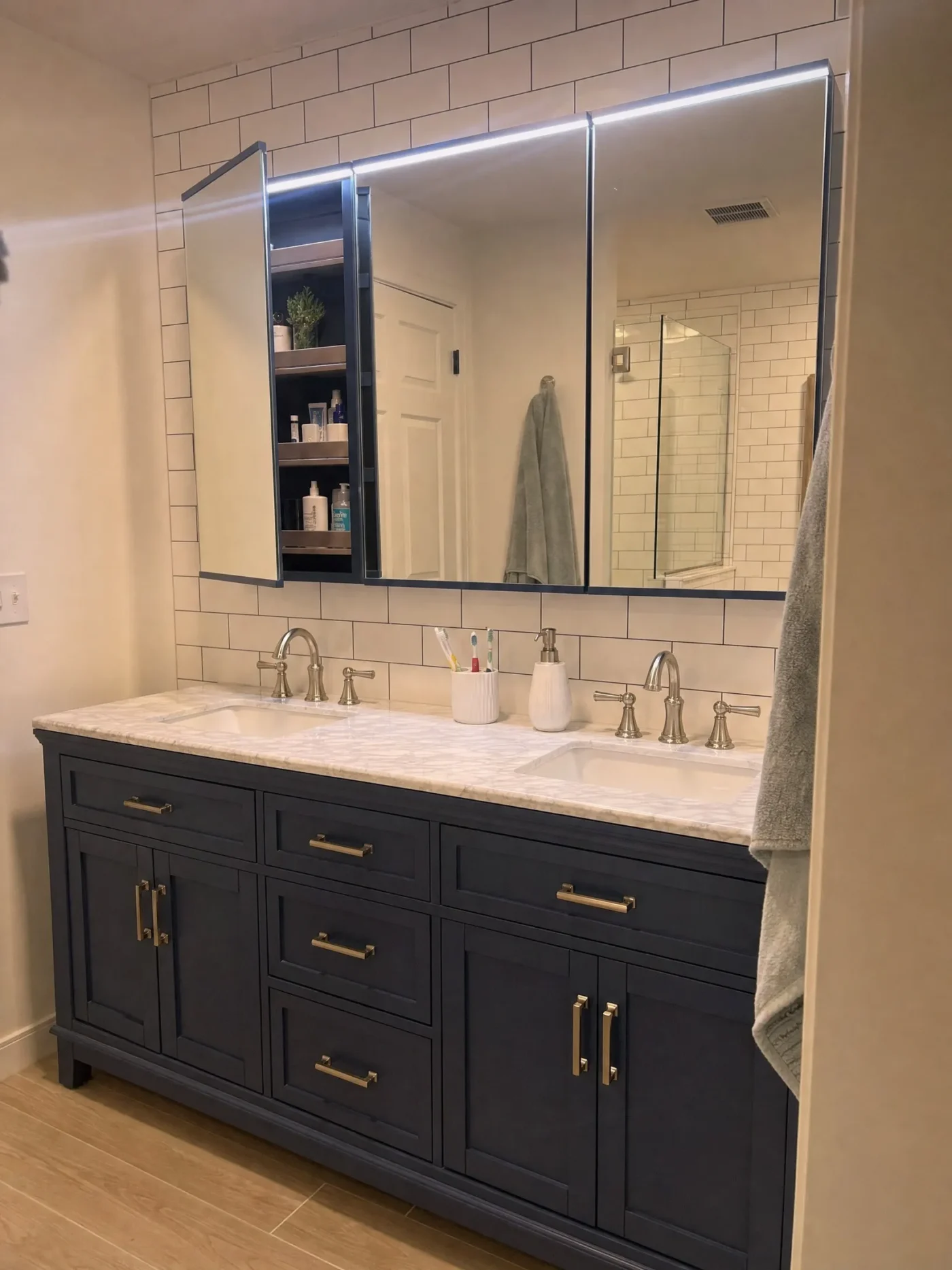 Triple medicine cabinet mirrors with LED lighting above gray blue double vanity with marble countertop in Dunedin FL coastal bathroom by CMK Construction