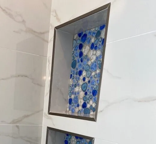 Shower niche framed with brushed nickel metal edge profiles and blue pebble tile in a Land O Lakes remodel by CMK