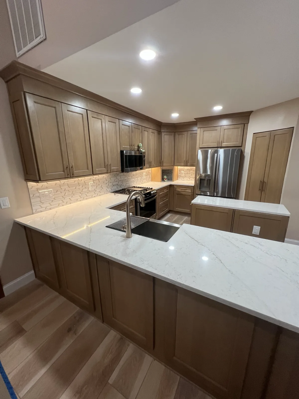 Finished Odessa kitchen peninsula with white quartz, a stainless farmhouse sink, a champagne bronze faucet, and warm wood cabinets