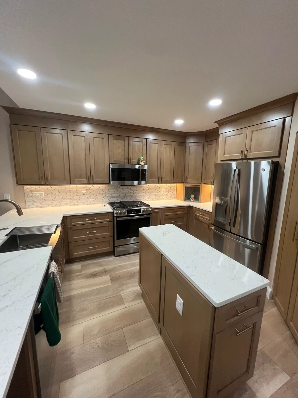 Finished Odessa kitchen center island and range wall with a gold pattern mosaic backsplash lit by under-cabinet LEDs