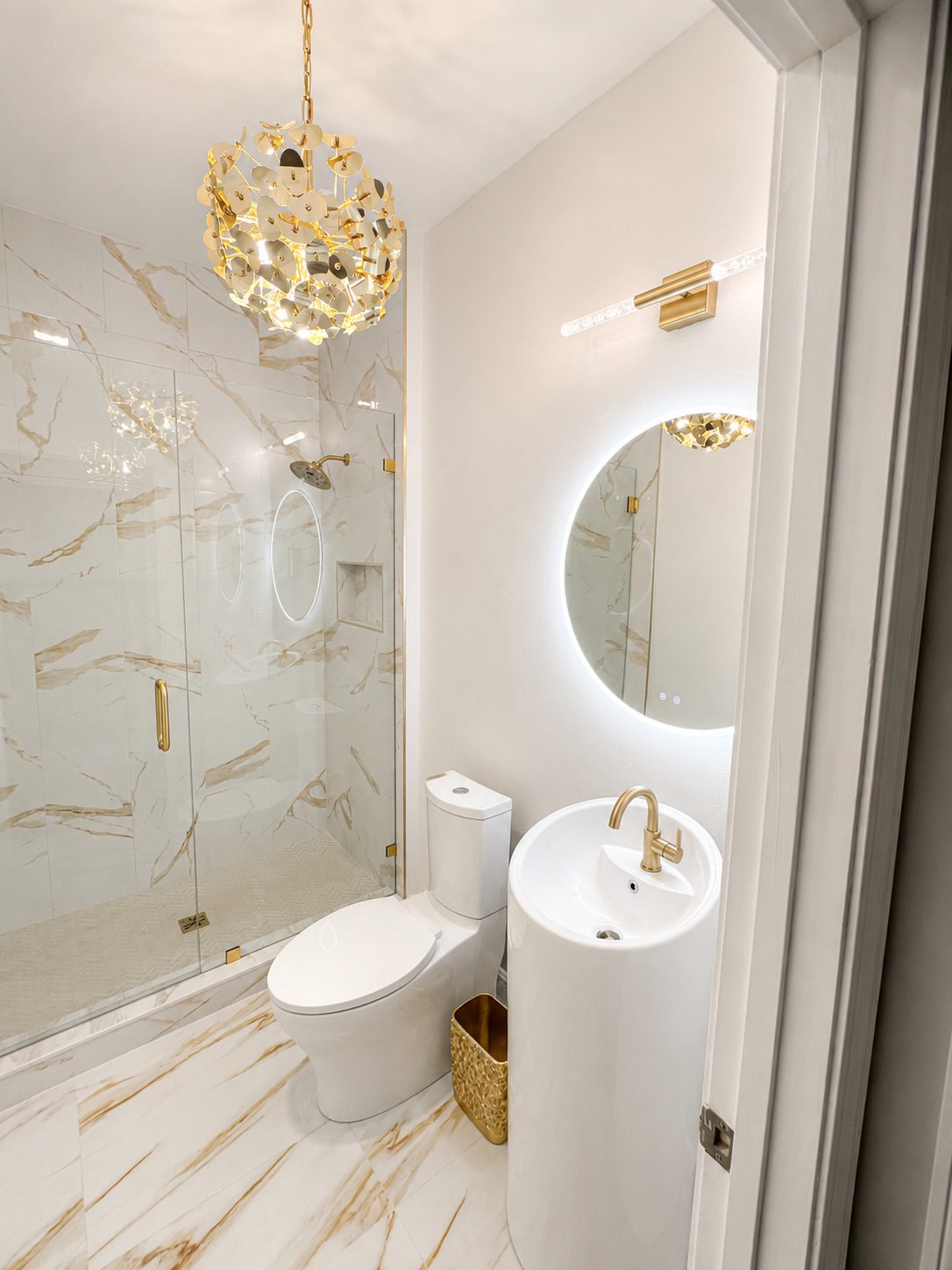 Round pedestal sink with brushed gold faucet and lighted round mirror in a Tampa powder room remodel