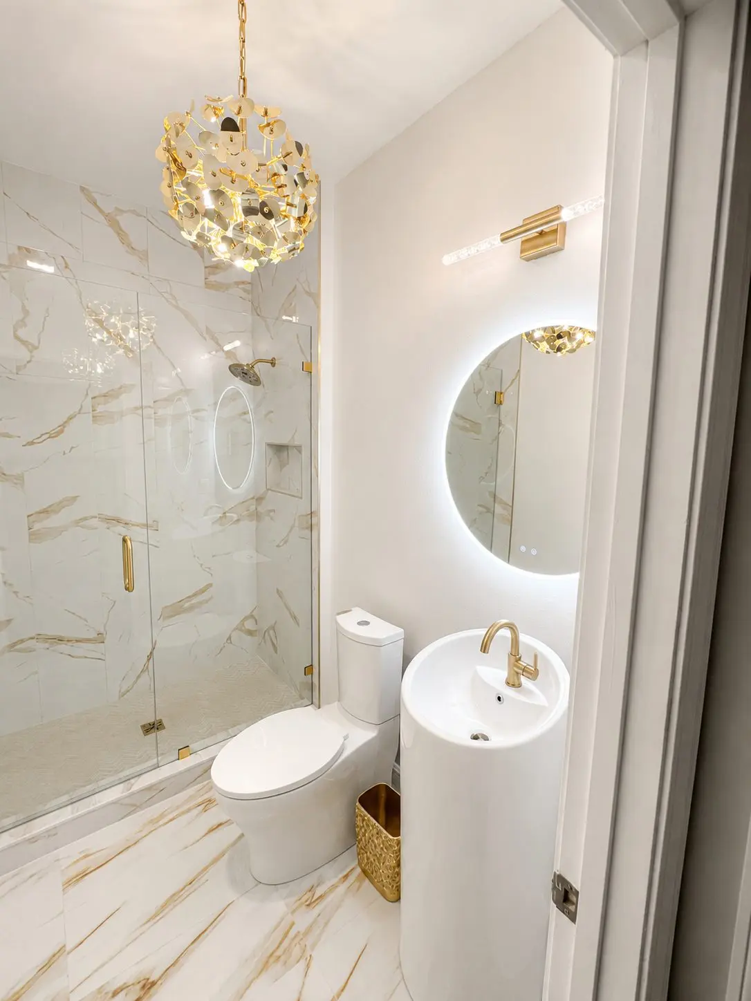 Round pedestal sink with brushed gold faucet and lighted round mirror in a Tampa powder room remodel