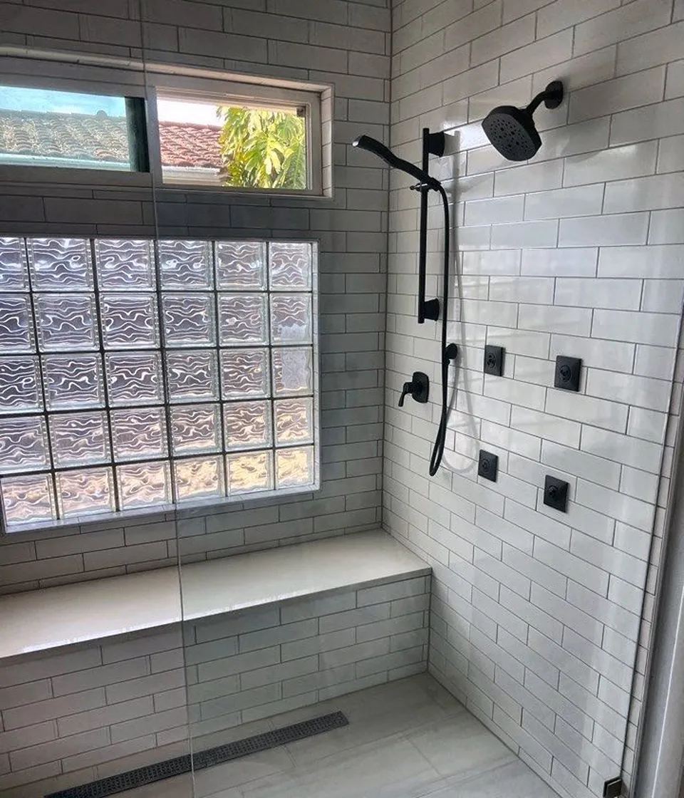 Full width shower bench with white quartz slab top under a glass block window with matte black fixtures in a St. Petersburg shower