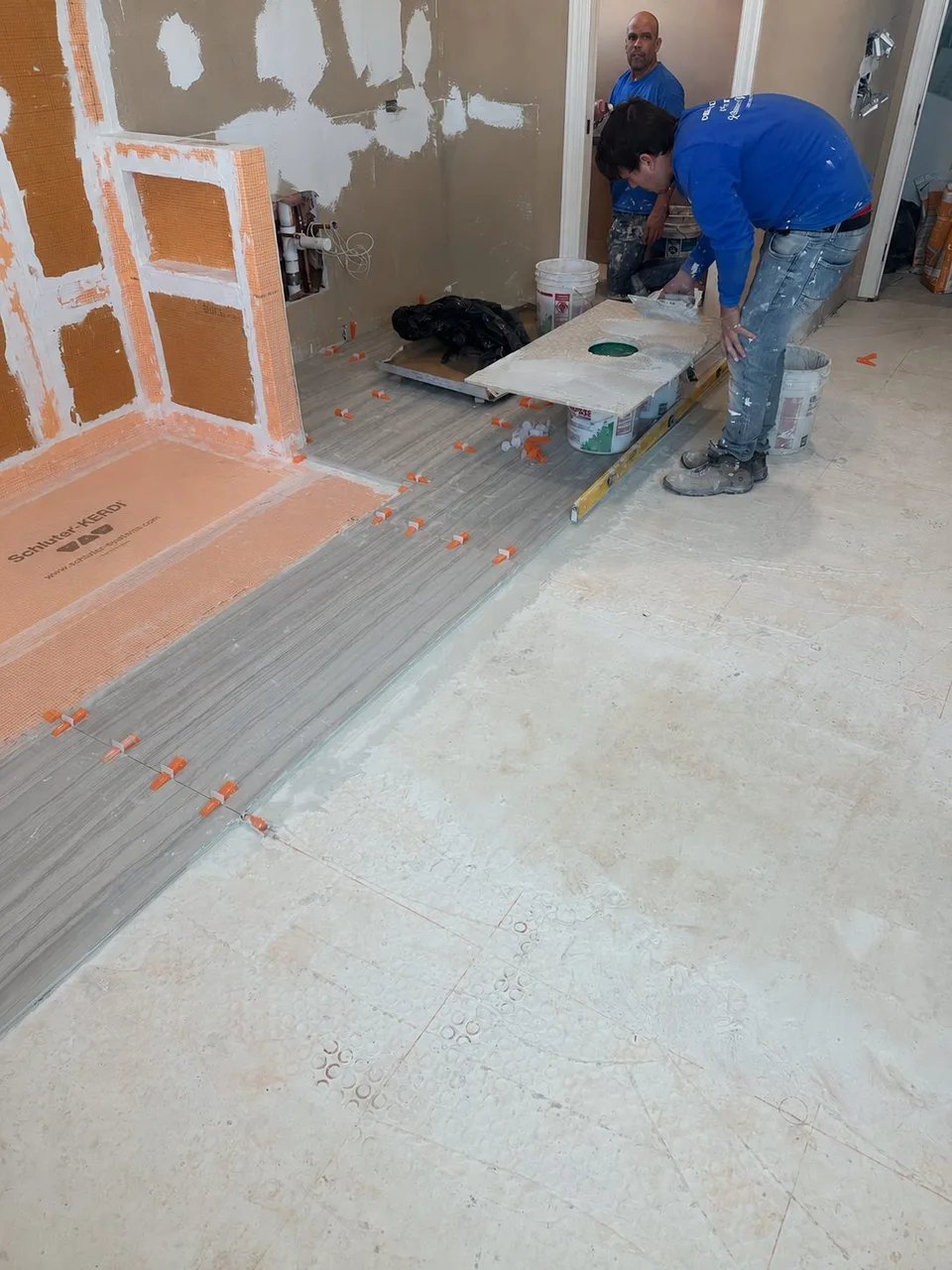 CMK Construction crew installing tile over a Schluter Kerdi shower pan with Kerdi Board bench and niche in a Tampa master bathroom remodel