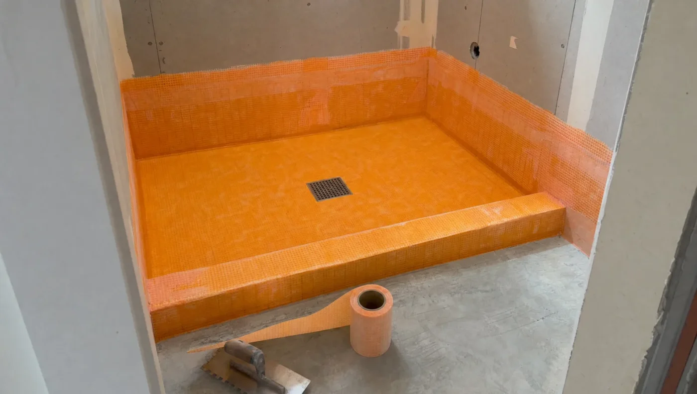 Pre-sloped foam shower tray covered in orange waterproofing membrane with a square center drain and wrapped curb, ready for tile