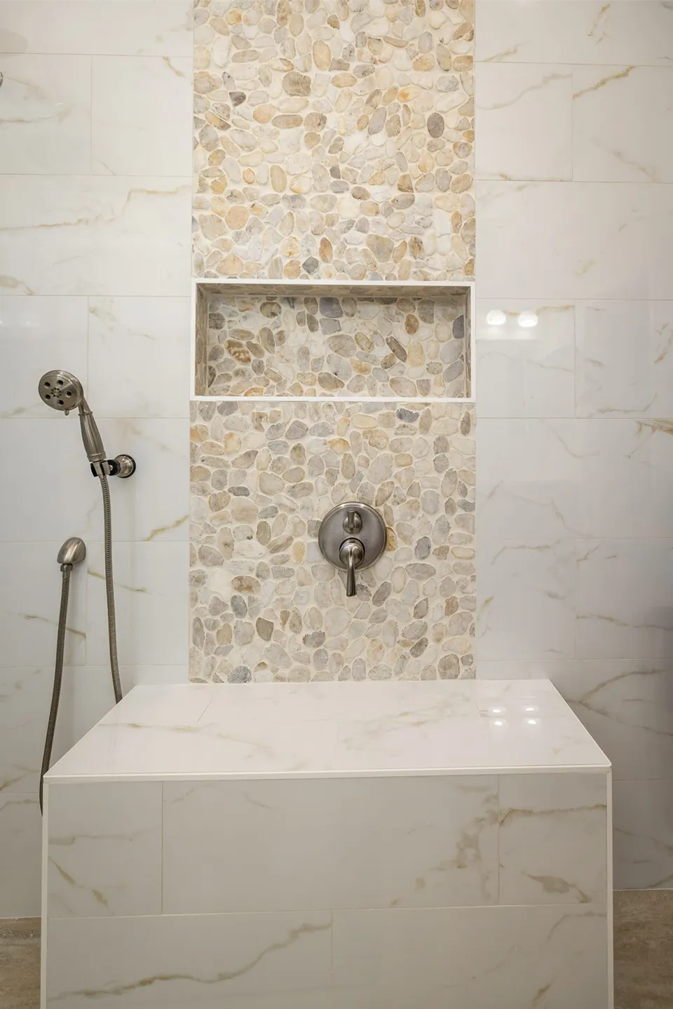 Shower bench in calacatta look porcelain against a floor to ceiling pebble mosaic accent column with recessed niche in a Clearwater shower
