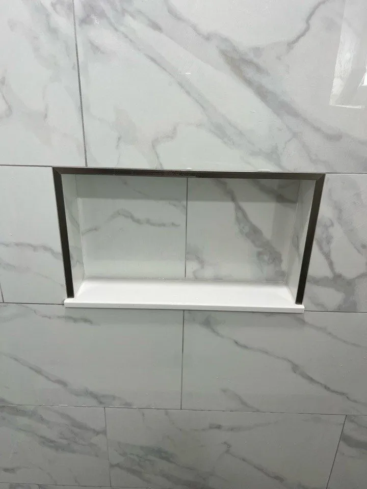 Shower niche with a solid quartz sill and metal trim edges in marble look porcelain, Dunedin bathroom remodel by CMK